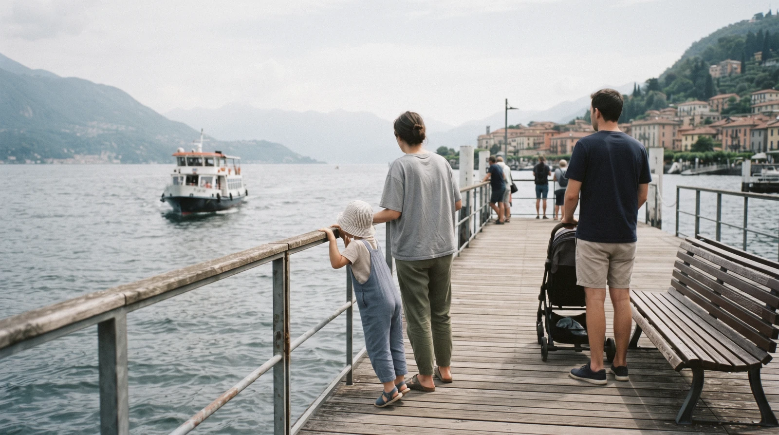 Children on the open upper deck of a slow lake boat watching a village pass, the everyday shape of Lake Como with kids